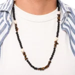 Thales è una collana da uomo realizzata a mano in Italia con pietre naturali di qualità, che donano un tocco di stile e personalità al tuo look, un accessorio che incanta per la sua moderna raffinatezza. Intrecciata con pietra lavica dall’aspetto poroso che contrasta con l’aulite bianca, questa creazione esclusiva, grazie anche all’occhio di tigre, evoca un senso di avventura e mistero.<br /> Queste pietre hanno anche dei significati simbolici: la pietra lavica rappresenta la forza e la trasformazione, mentre l’occhio di tigre stimola la fiducia e la protezione.<br /> Questa collana si abbina con naturalezza a outfit casual e sportivi e anche con colori caldi e neutri. È perfetta per le vacanze estive o per regalare un tocco casual al tuo look quotidiano in tutte le stagioni. ndossa Thales e lasciati trasportare in un viaggio di stile e libertà, dove ogni dettaglio racconta una storia senza tempo. <ul class="testo-prodotti"> <li class="spaziatura"><strong>Materiali</strong>: Minuterie e chiusura placcate argento 5 micron, ciuffo di bandana in cotone</li> <li class="spaziatura"><strong>Pietre</strong>: Pietra lavica con taglio a perla, aulite bianca a sasso e chips di occhio di tigre marrone</li> <li class="spaziatura"><strong>Taglia Unica</strong>: La lunghezza totale della collana è di 70cm</li> <li class="spaziatura"><strong>Chiusura</strong>: Con moschettone</li> <li class="spaziatura"><strong>Confezione</strong>: La collana è venduta all’interno di un’elegante scatolina con logo Dandy Street. Perfetta anche come regalo!</li> </ul>